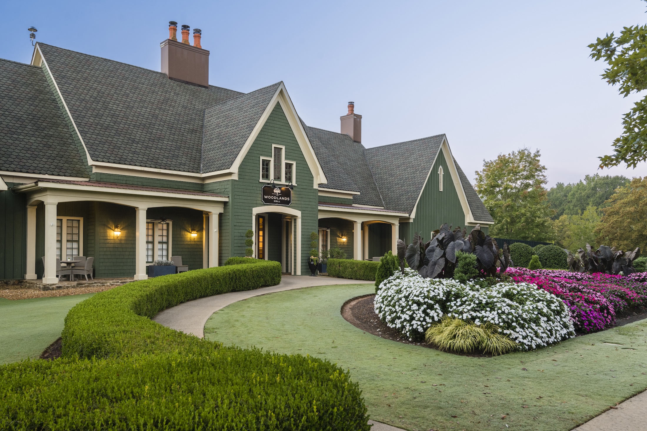 The exterior of Woodlands at Barnsley Resort. A green building with a lush garden in front of it.