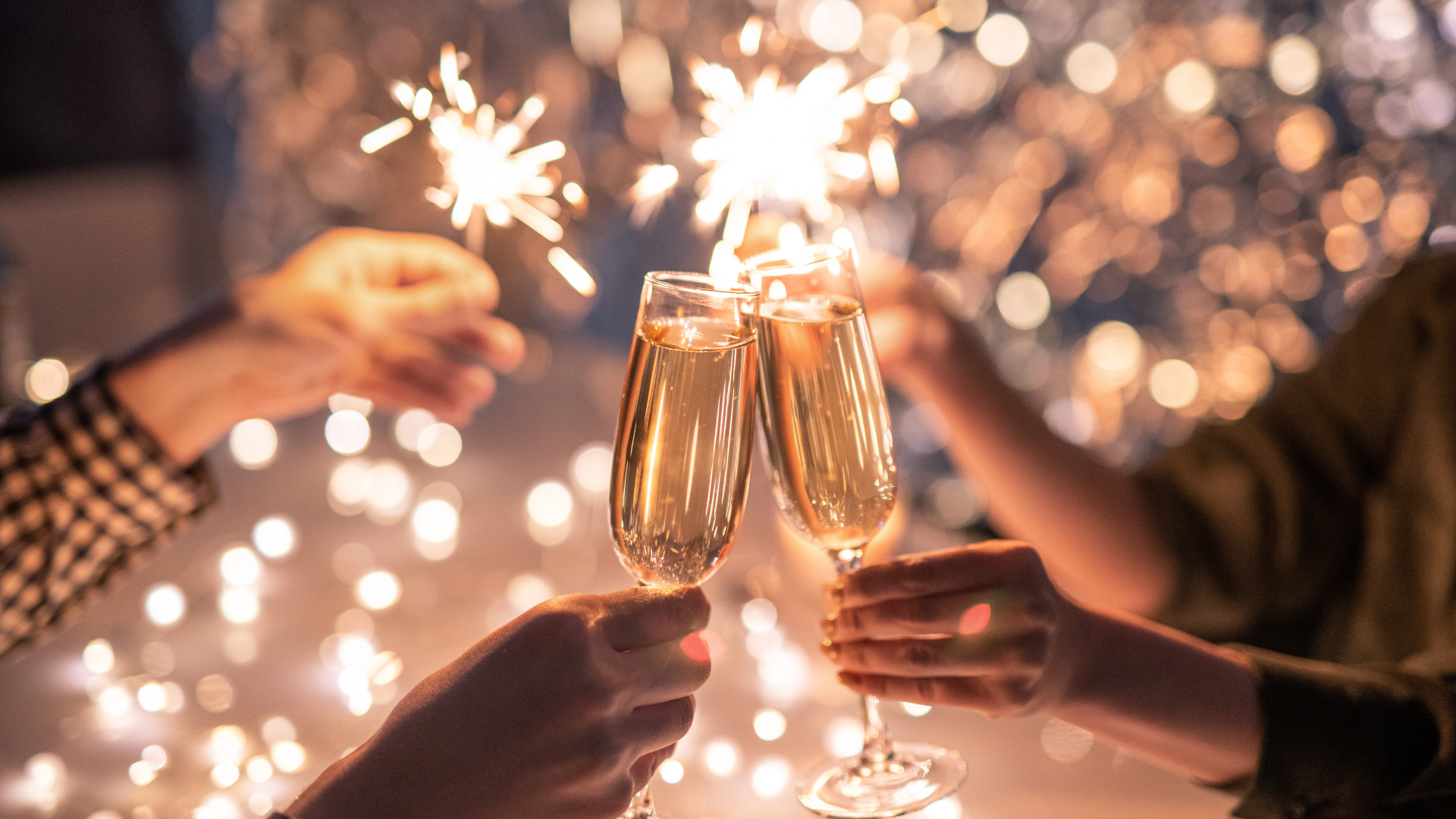 two hands clinking champagne glasses, sparklers in background