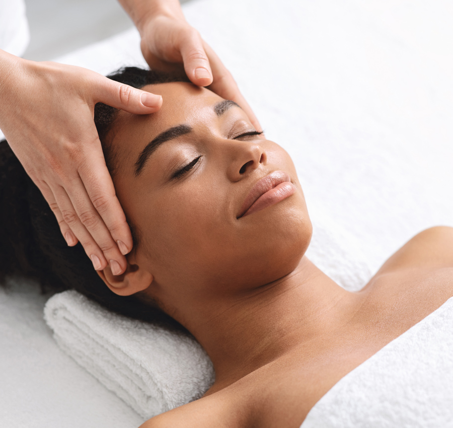 A spa worker gives a woman a light facial massage with both hands.