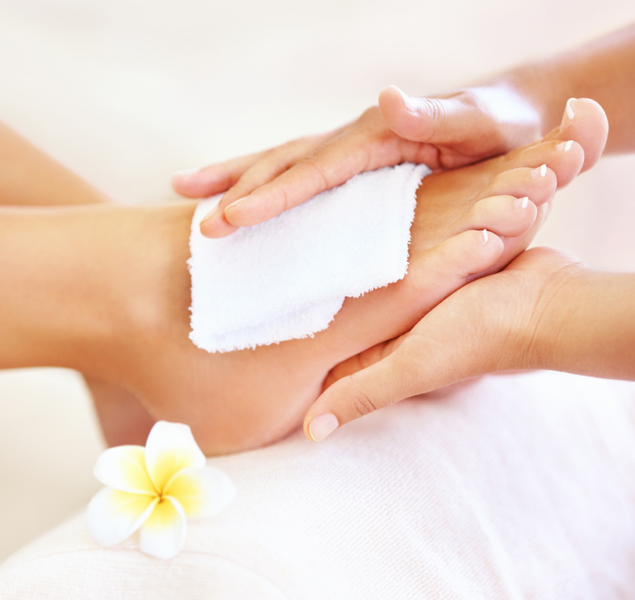 A spa worker uses a cloth to provide spa treatment to a woman's foot.