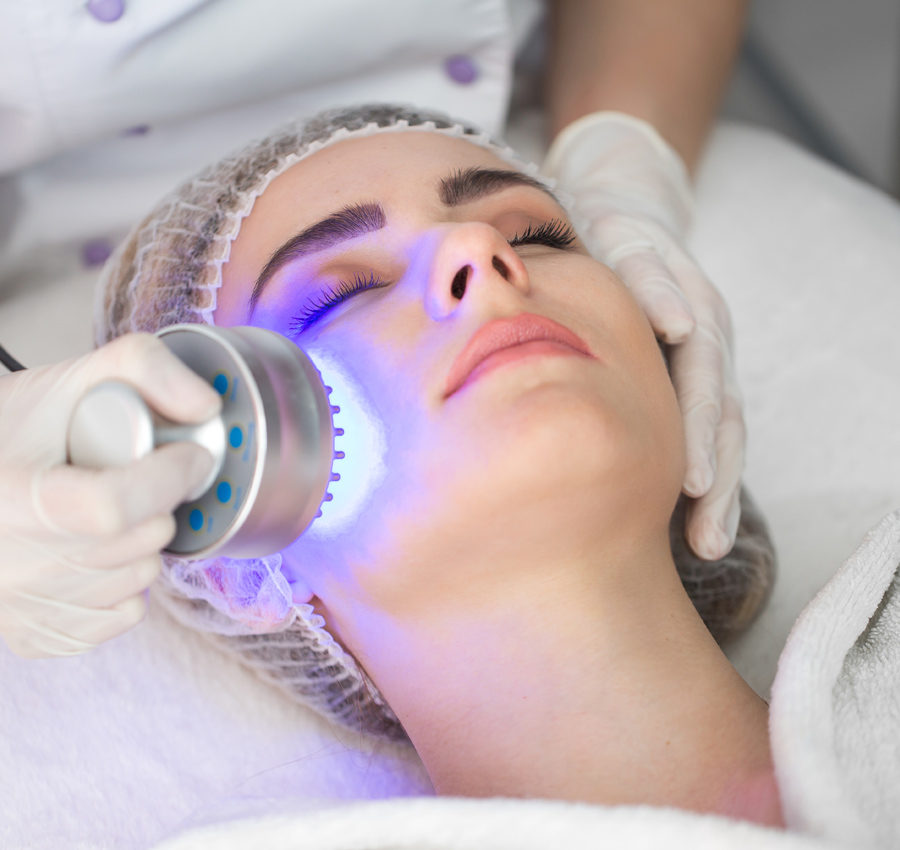 A woman is receiving LED therapy during her facial. A bright purple light is emitted from the tool being used by the spa worker.