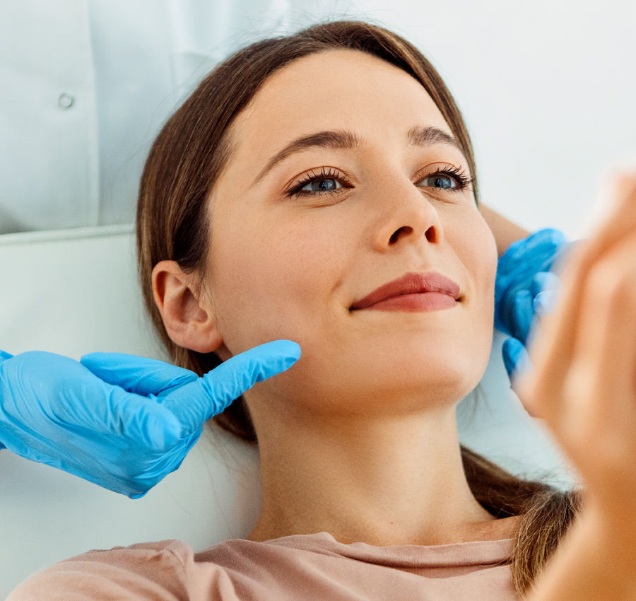 A spa worker wearing blue gloves shows a woman the results of her lip treatment in a spa.