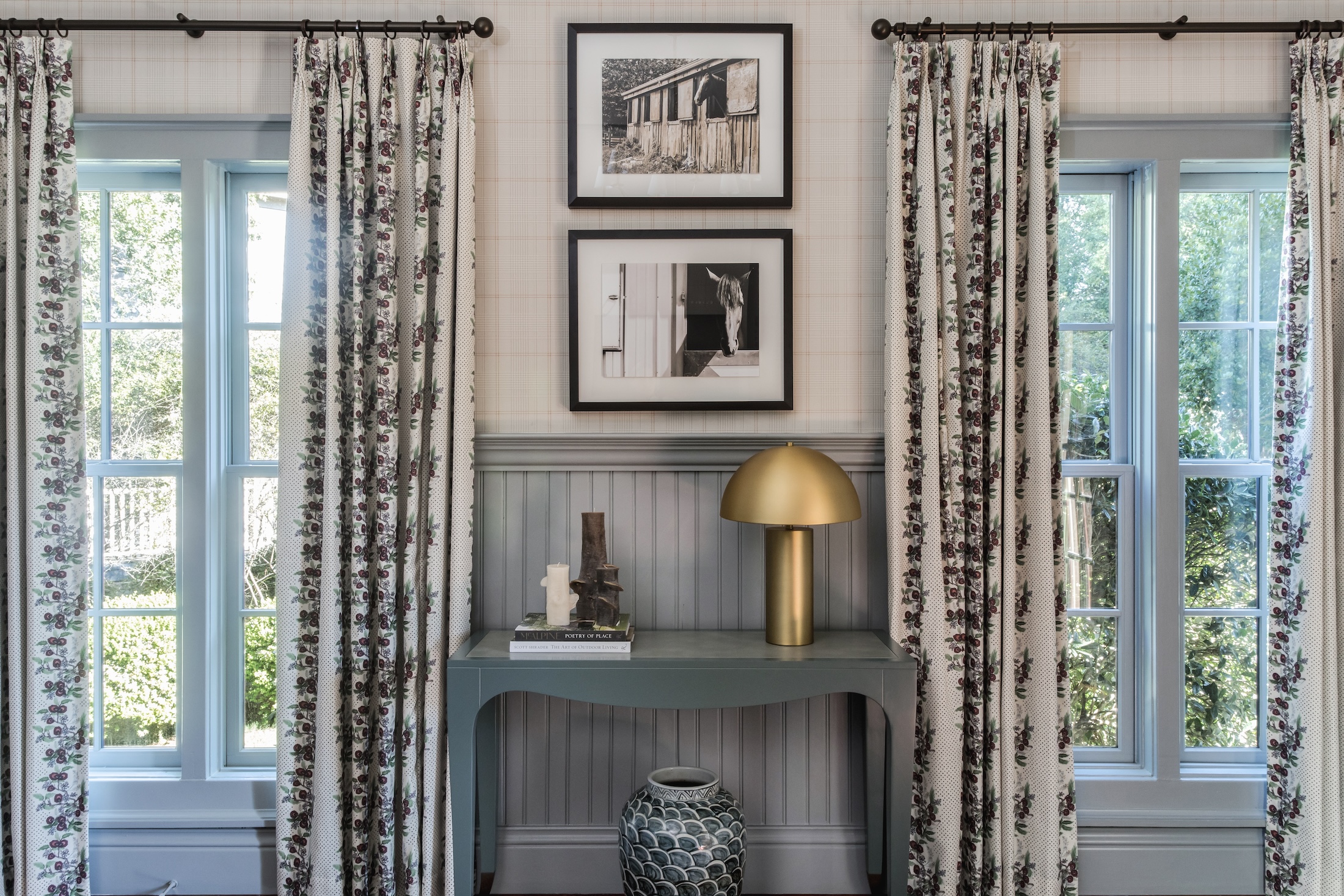 A side table with golden lamp and artwork framed by two windows in Arbor Cottages at Barnsley Resort.