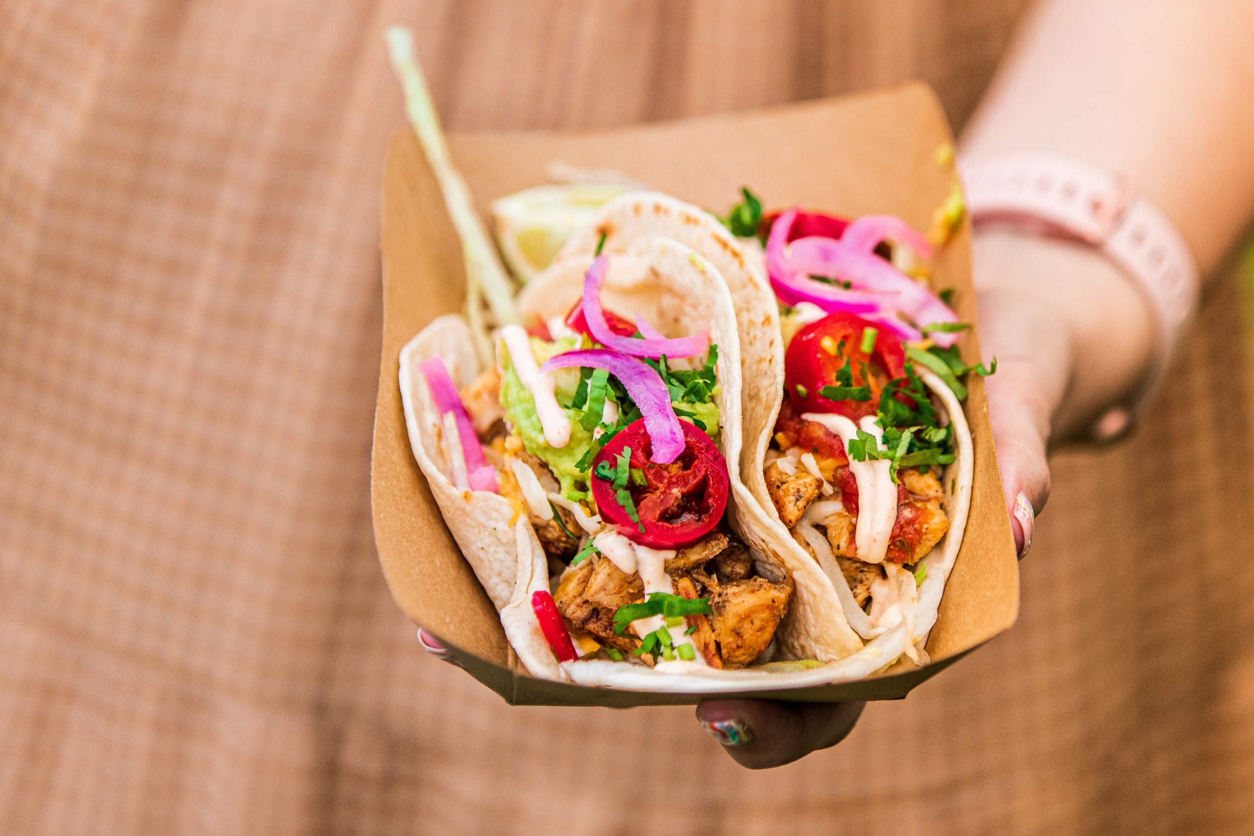 woman hand holding a tray of street tacos