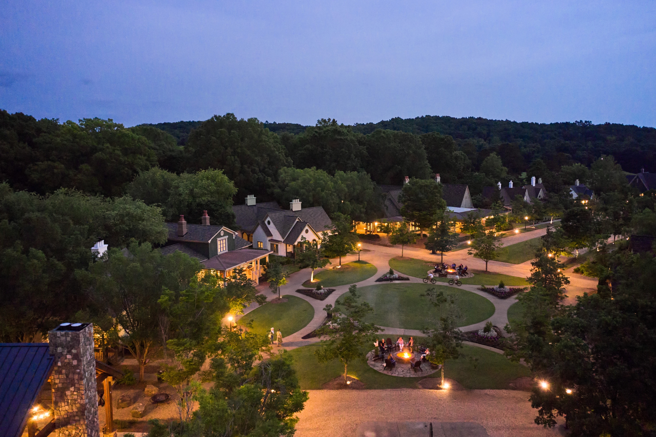 A resort village of cottages at dusk. Firepits line the sidewalks.