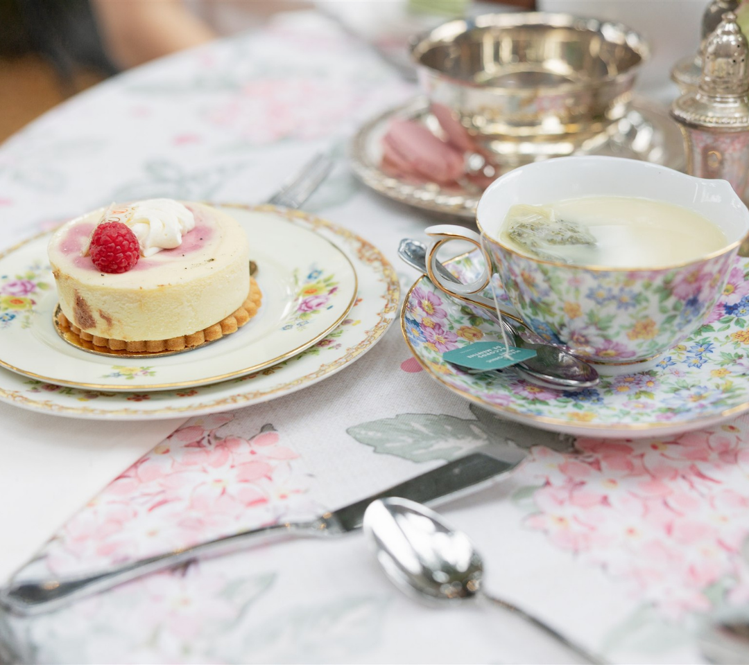A cup of tea and plated pastry on a floral print table with flowers and silverware