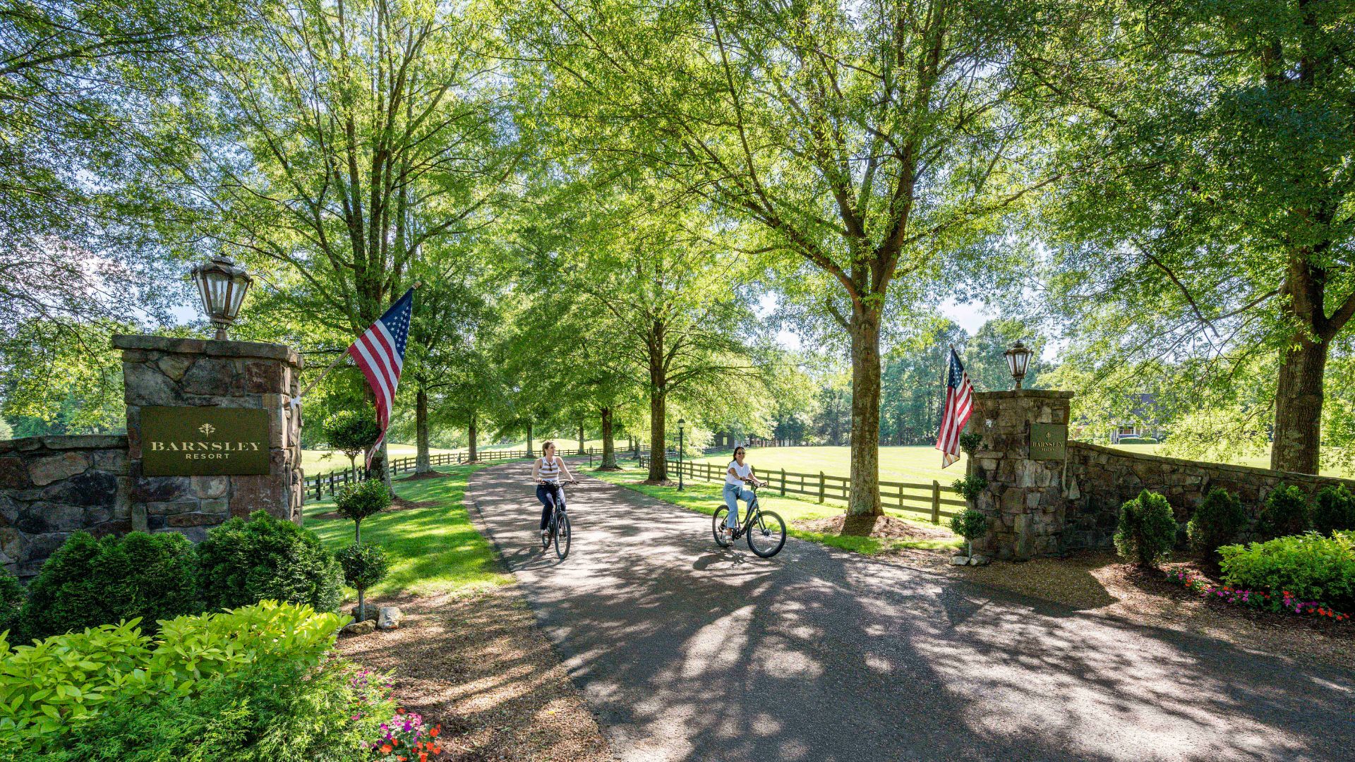 two women on bikes at a resort entrance with American flags