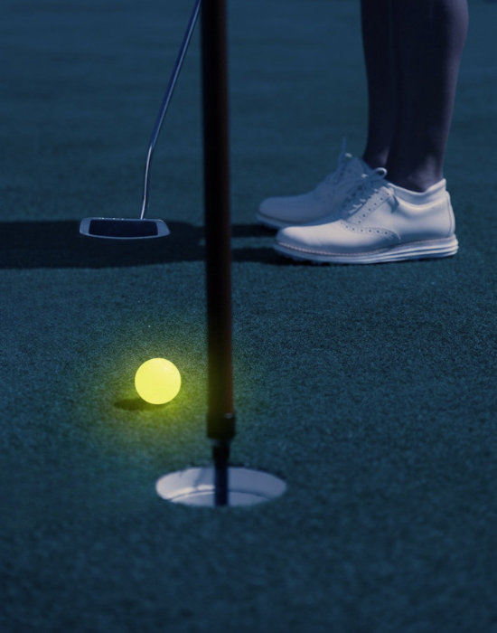 A nighttime image of a person with a putter and a glow in the dark golf ball.