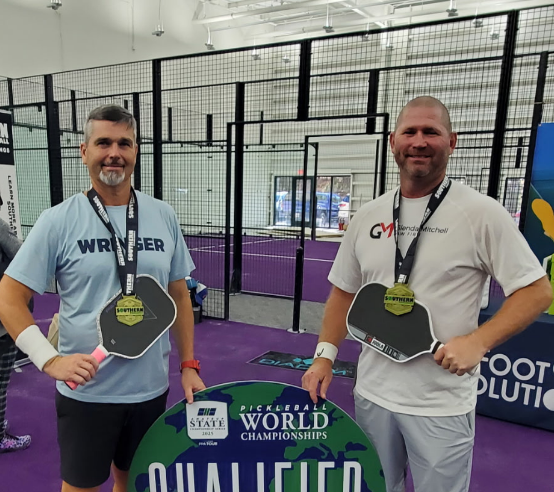 two men holding a sign with pickleball paddles