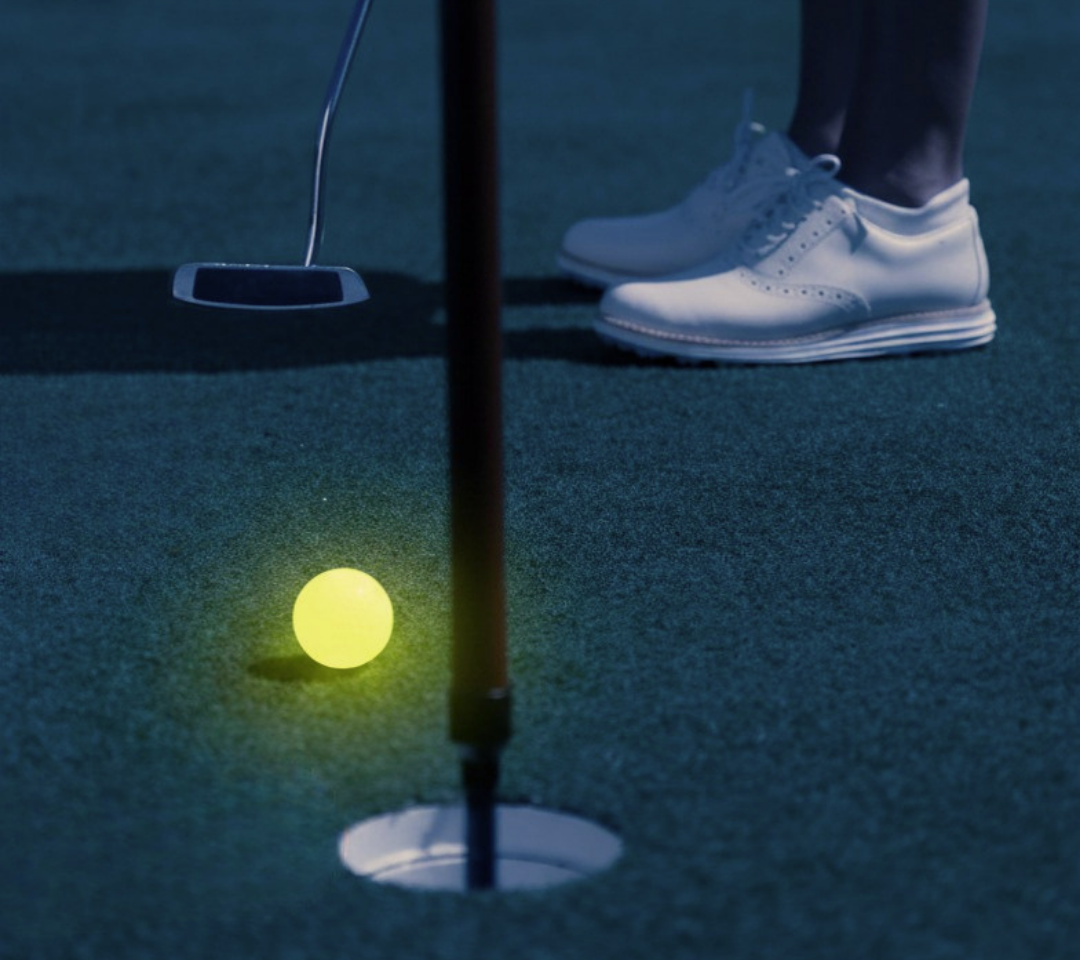 A nighttime image of a person with a putter and a glow in the dark golf ball.