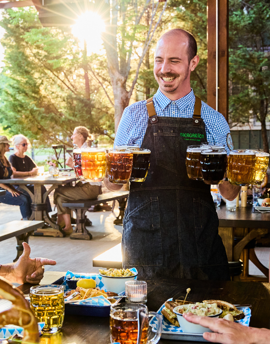 man smiling and holding beers in front of table of diners