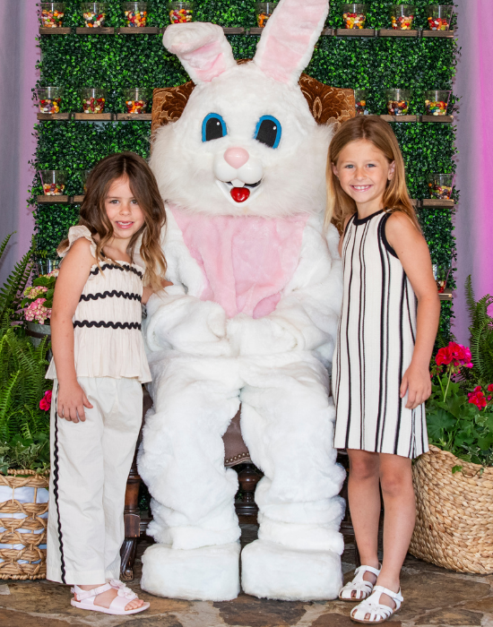 two girls stand with a person in an easter bunny costume with florals and decorations for easter