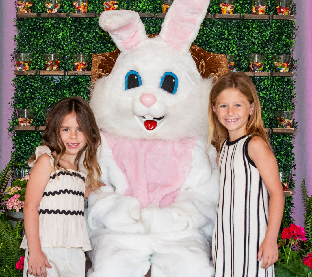 two girls stand with a person in an easter bunny costume with florals and decorations for easter
