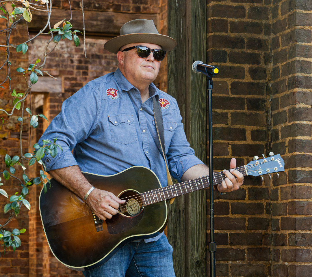 Man holding and playing guitar in a brick building
