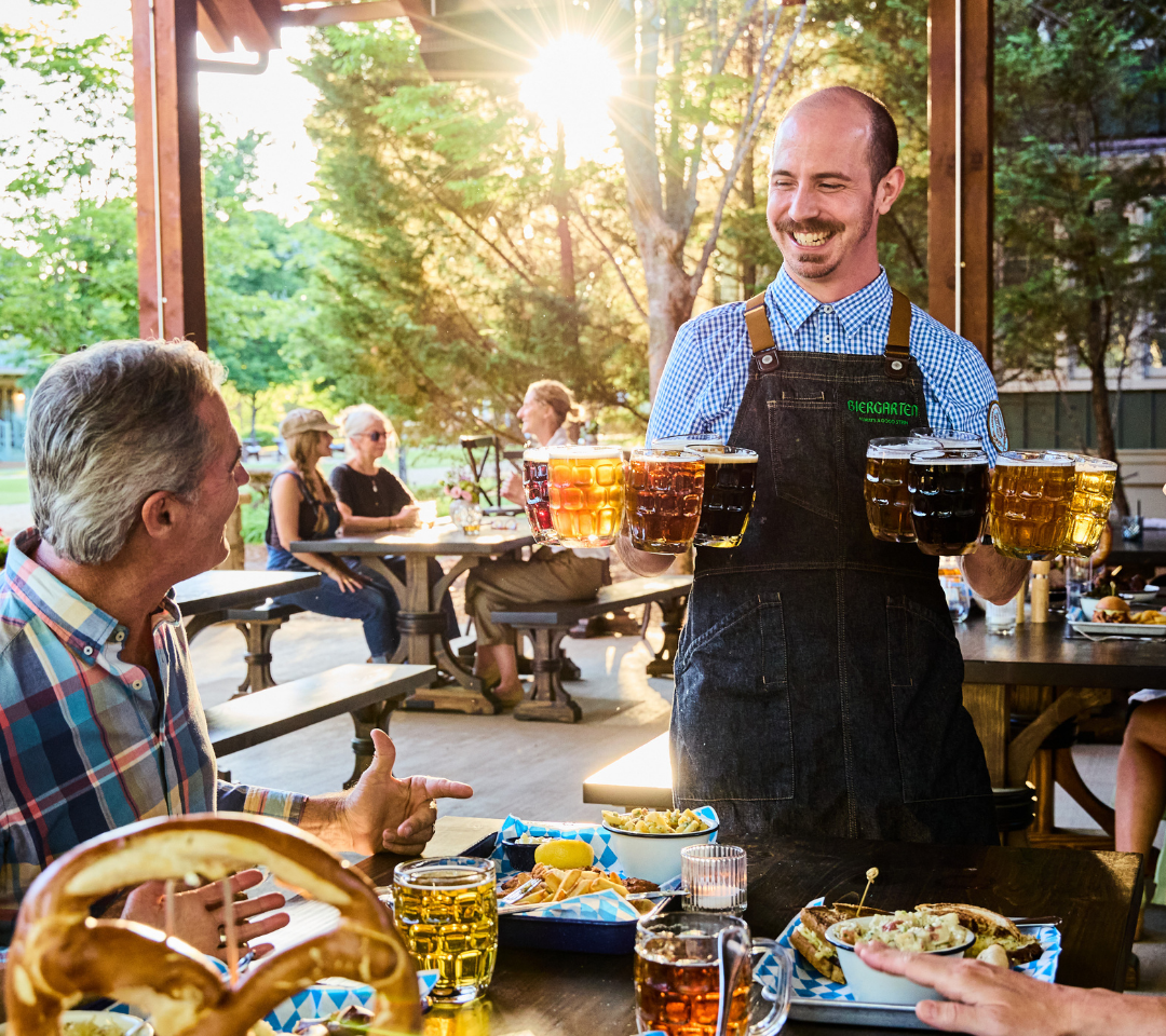 man smiling and holding beers in front of table of diners
