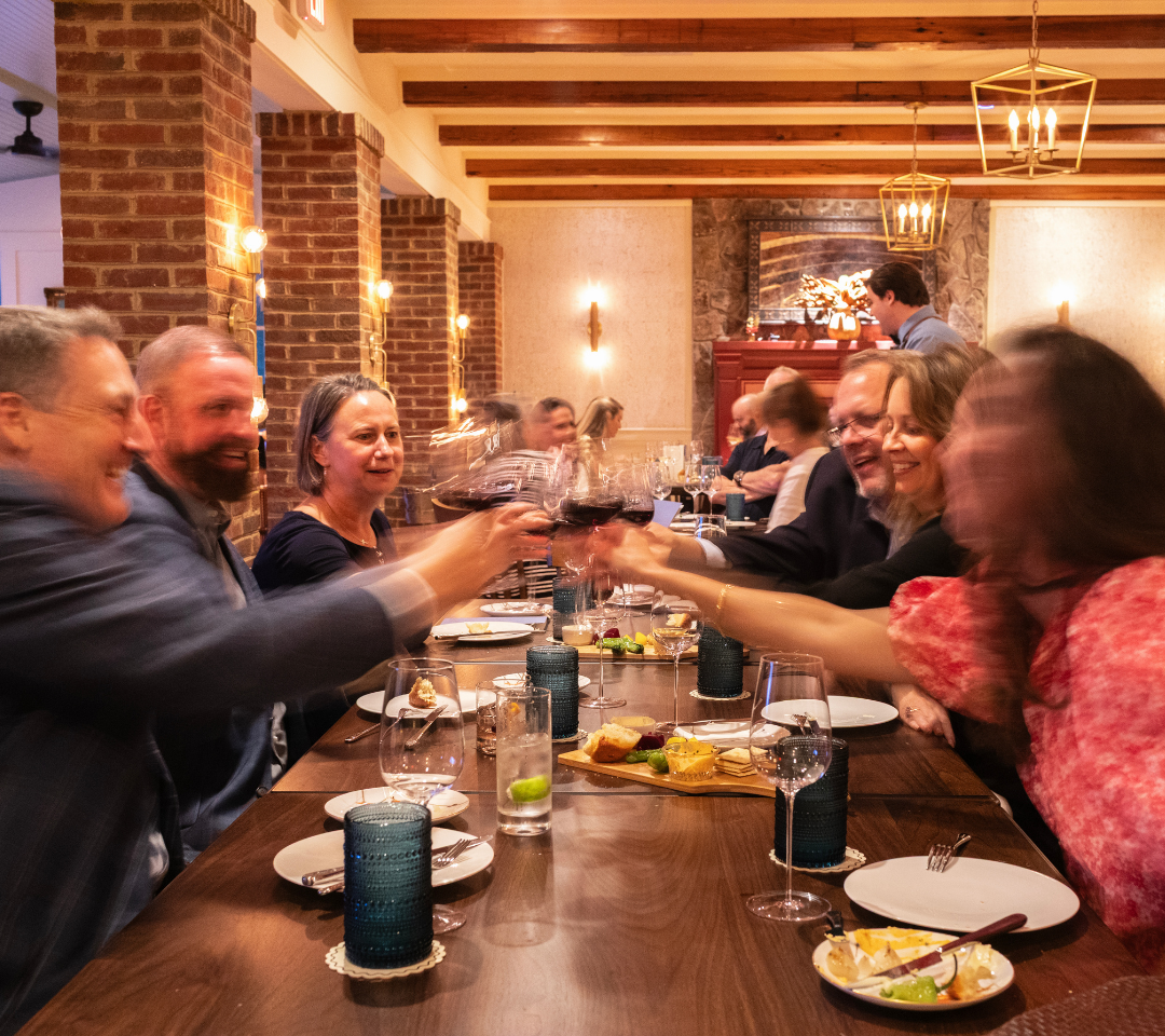 group of women and men around a dining table clinking their wine glasses.