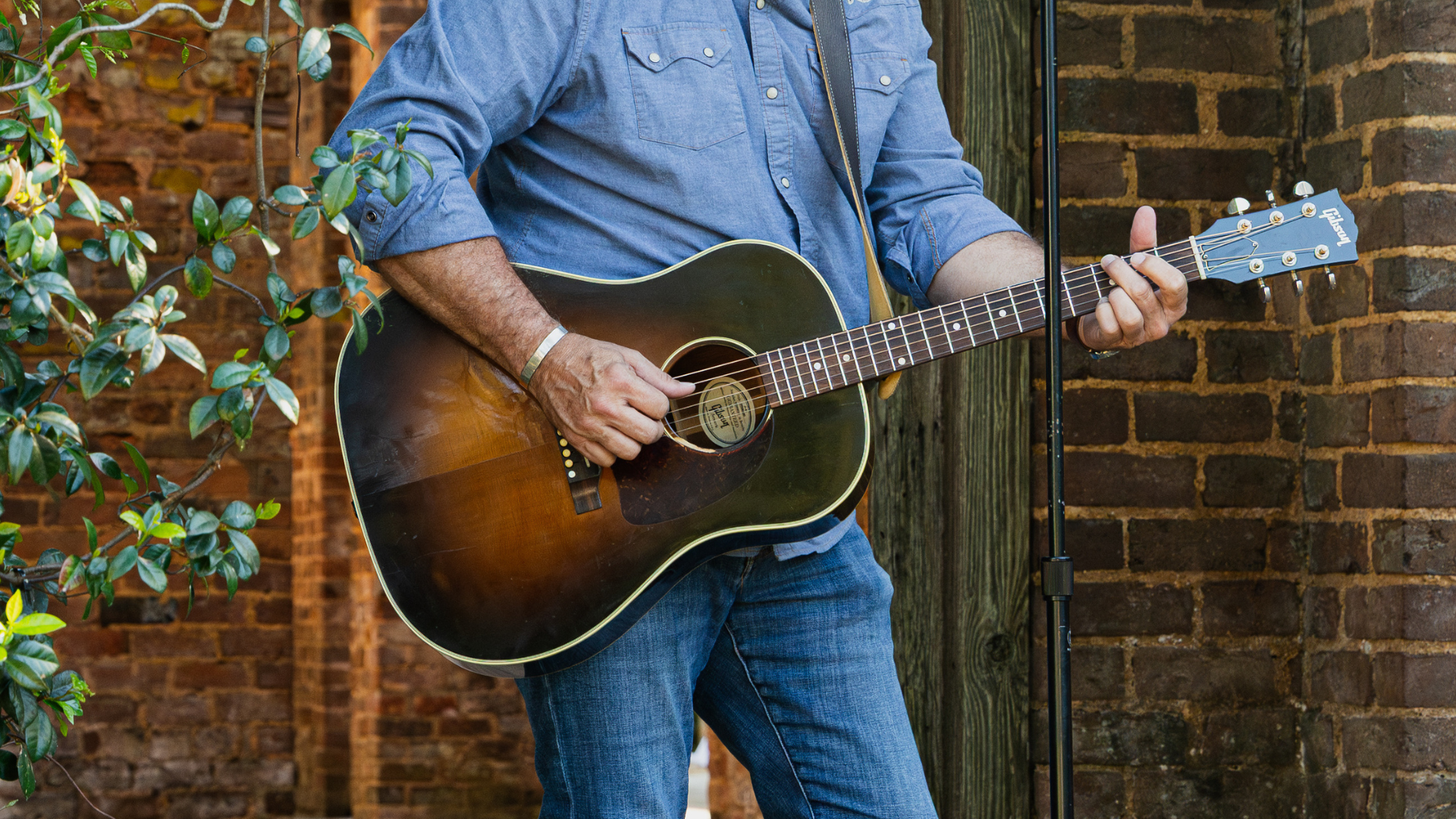 Man holding and playing guitar in a brick building