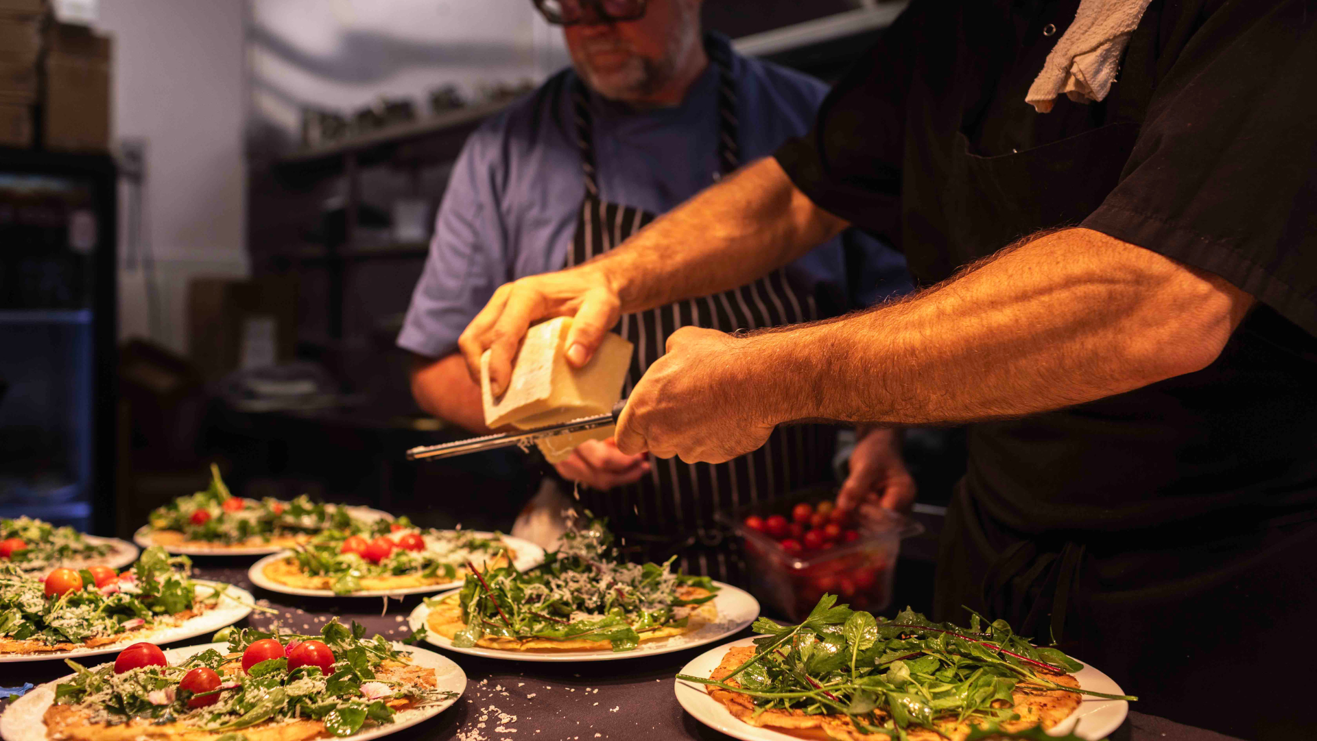 hands grating cheese over plates of salad