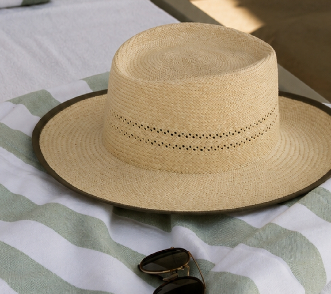 a hat sitting on a striped towel with sunglasses near it