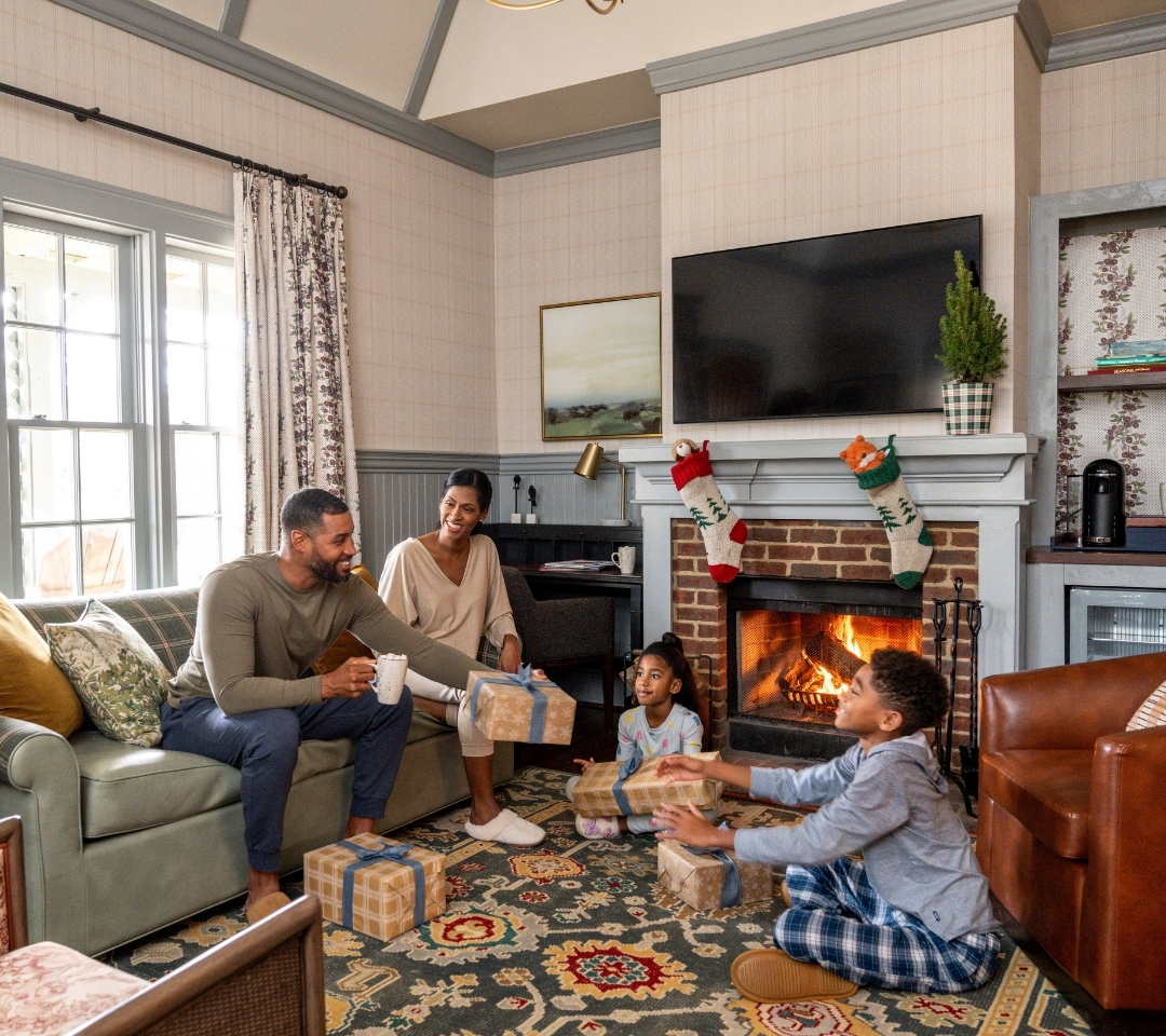 family sitting in living room passing Christmas presents to each other