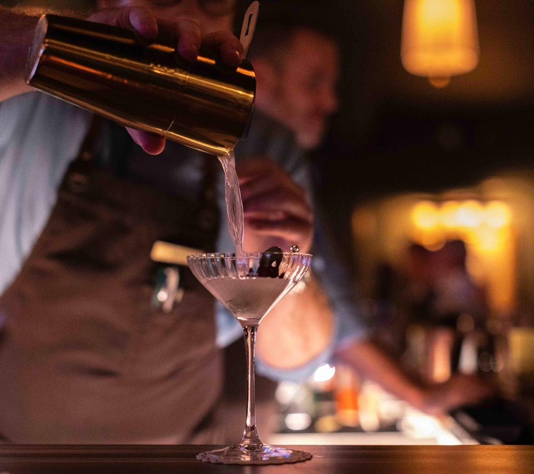 a man pouring a cocktail into a glass