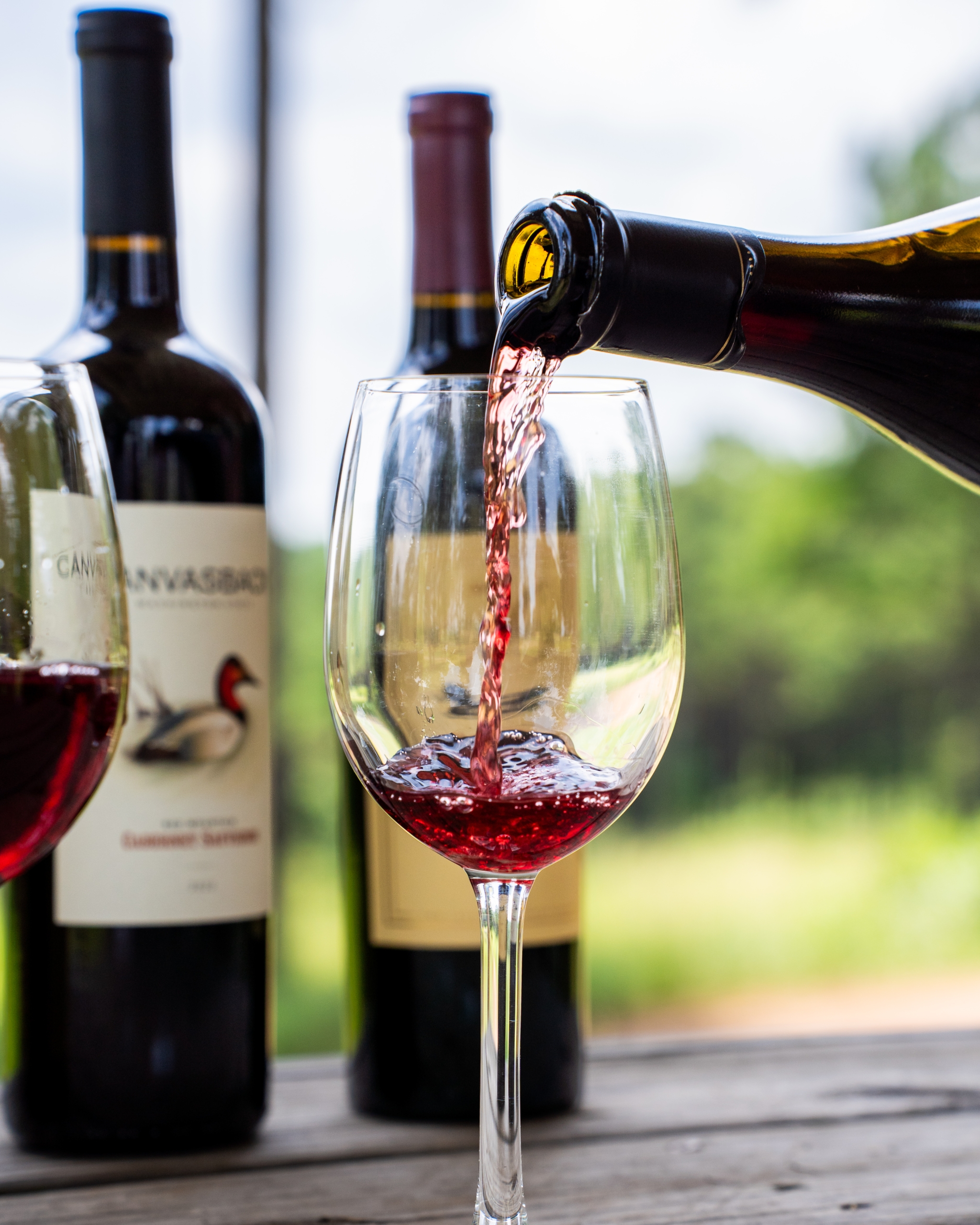 wine bottles behind a glass of wine being poured